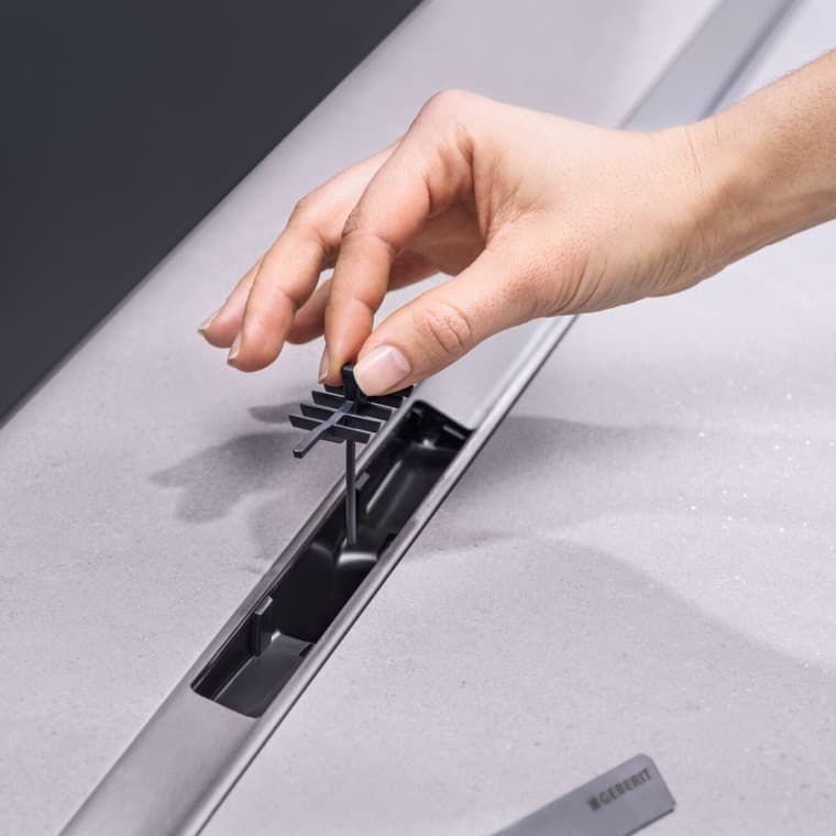 Hånd, der placerer en hårsi i afløbet Hånd, der placerer en hårsi i afløbet